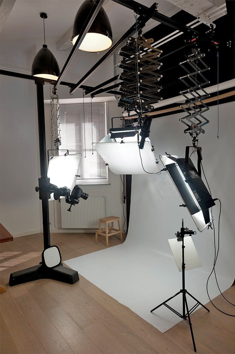 Plateau de studio photo avec fond blanc continu, flashs suspendus au plafond et pied colonne pour reflex