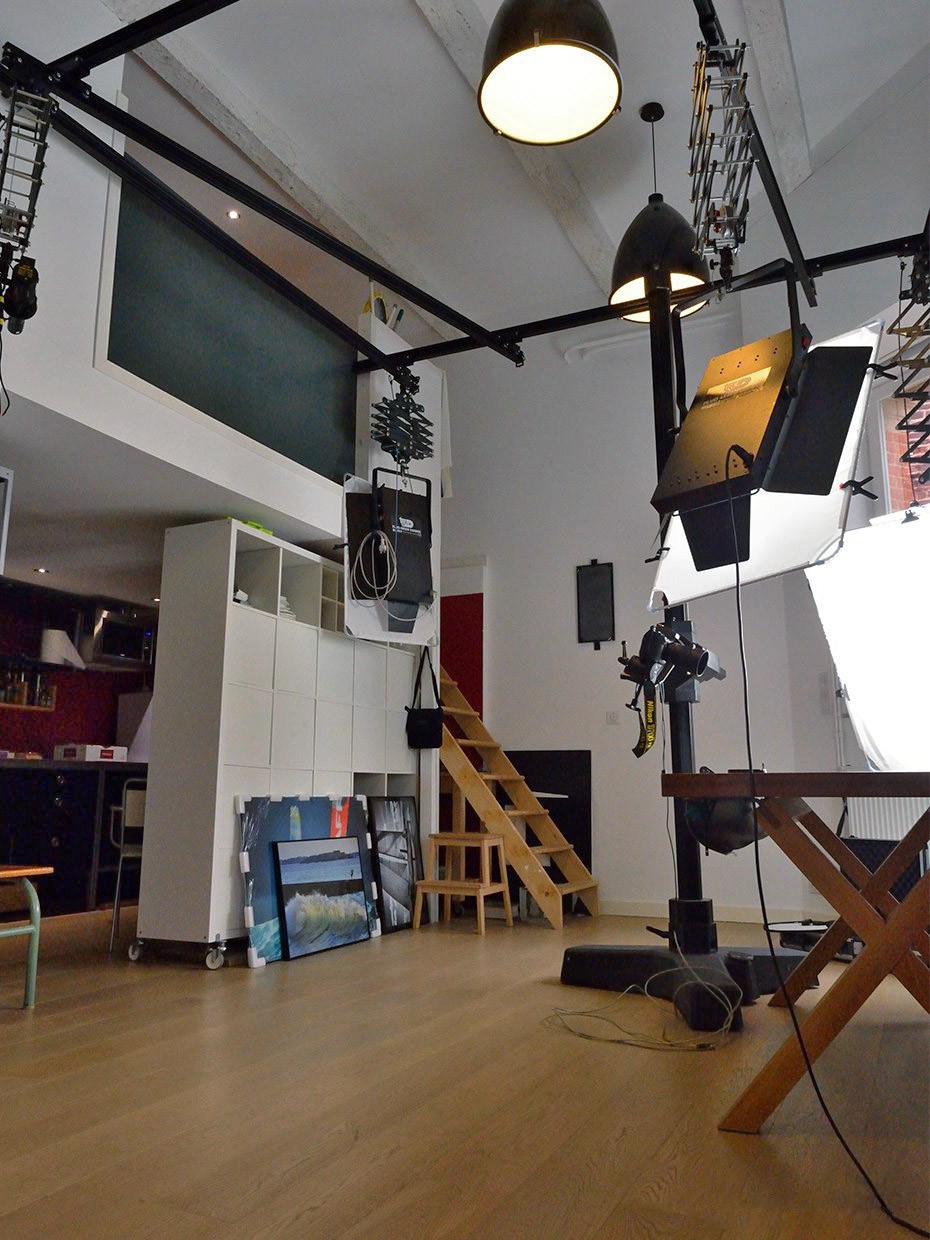 Studio photo culinaire en loft avec cuisine équipée en arrière-plan, meuble de rangement à cases, mezzanine et matériels d’éclairage