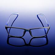 Monture de lunettes noire rectangulaire sur surface réfléchissante bleue avec dégradé lumineux en studio.
