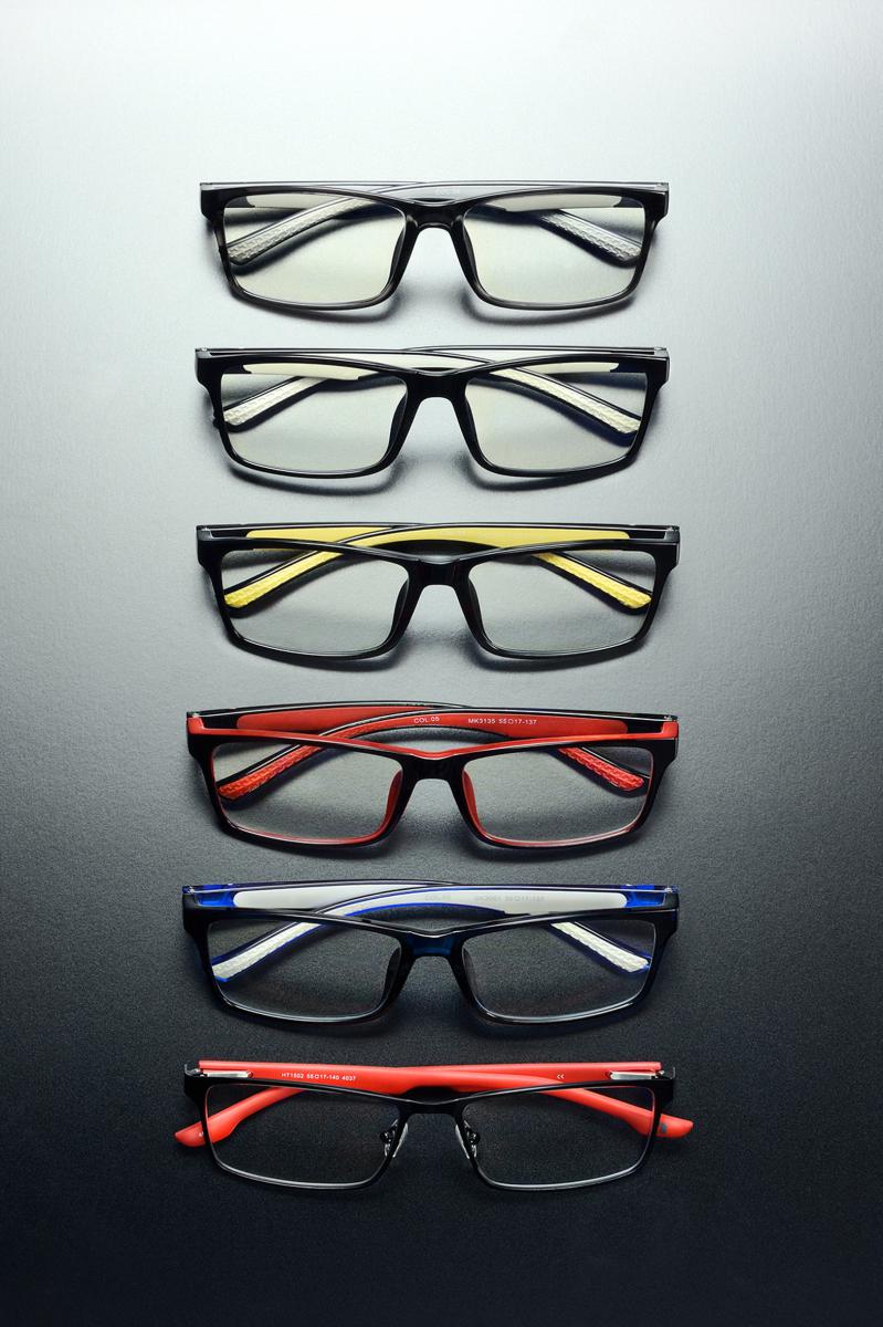 Alignement vertical de six paires de lunettes colorées sur fond gris dégradé avec éclairage studio précis.