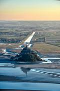Vue aérienne du Mont Saint-Michel et du Couesnon serpentant entre les bancs de sable sous une lumière de fin de journée.