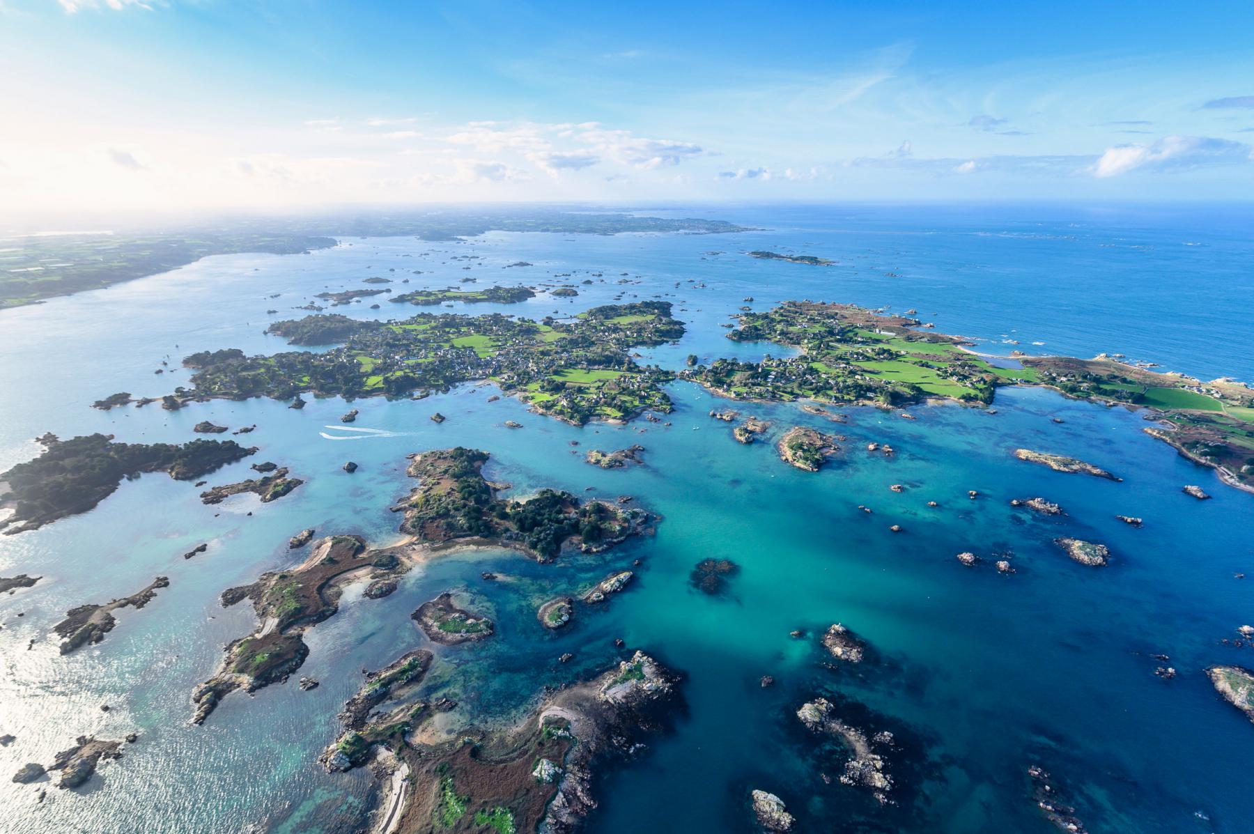 Vue en plongée sur les multiples îlots verdoyants de Bréhat entourés d’une mer turquoise sous un ciel bleu clair.