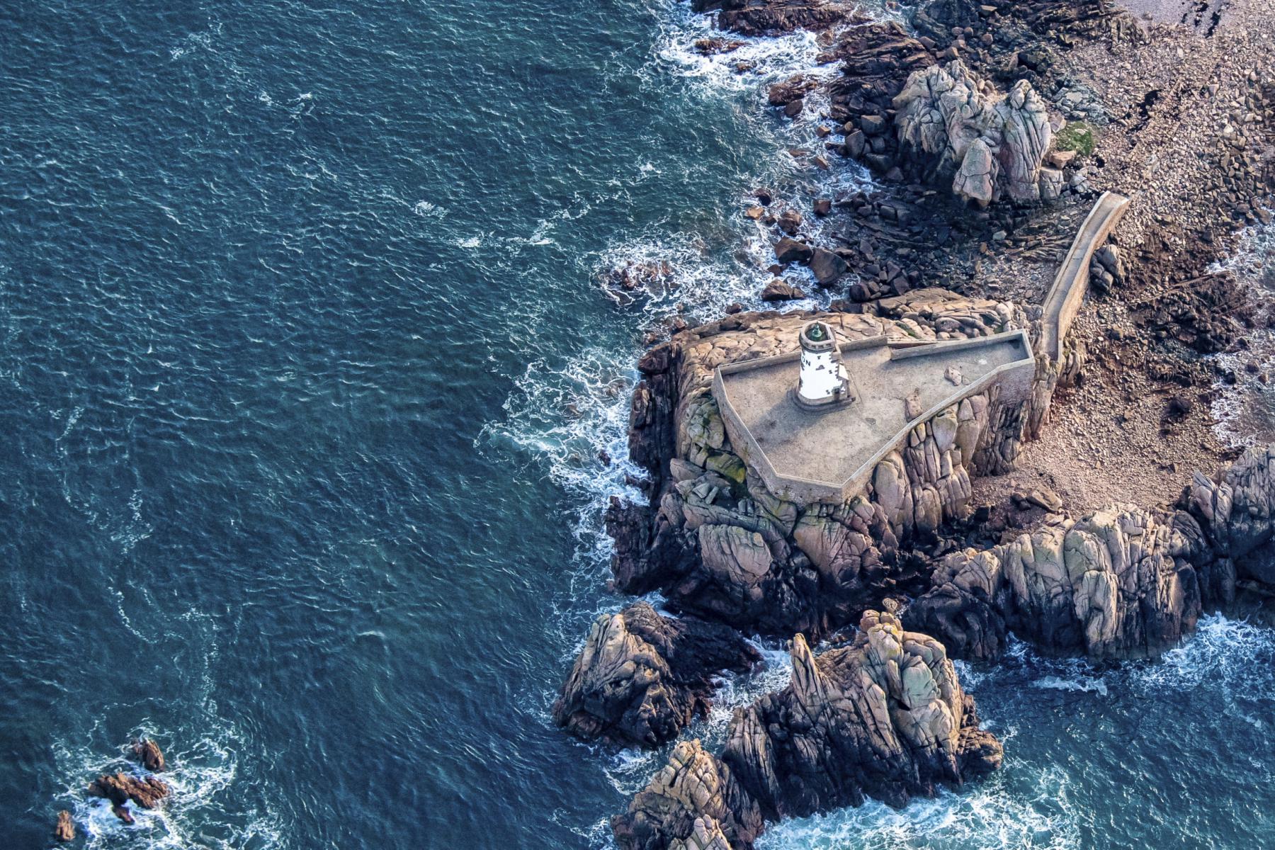 Vue aérienne du phare du Paon entouré de rochers de granit rose et de l’eau turquoise de la mer en Bretagne.