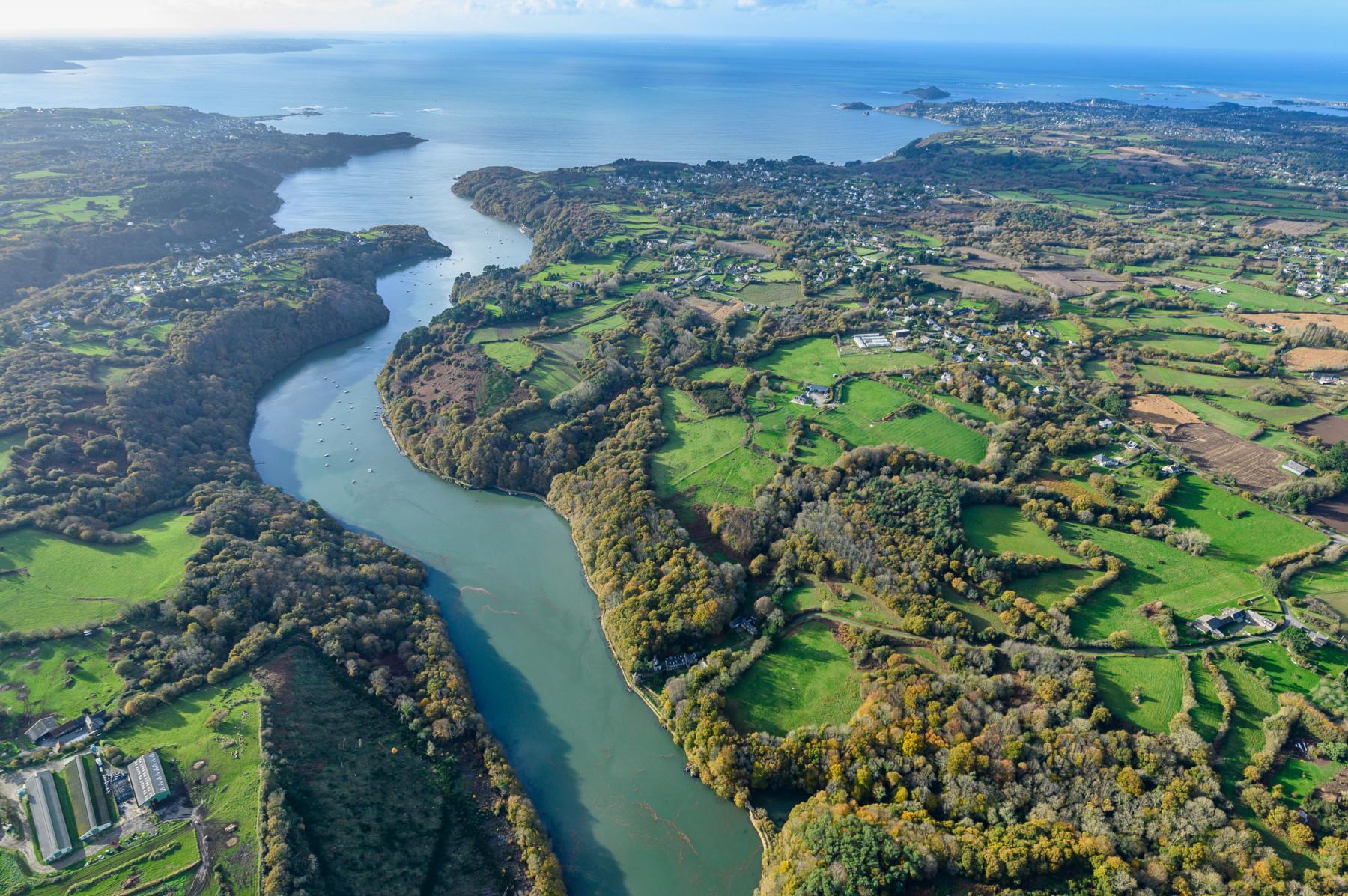 Vue du ciel du fleuve Jaudy serpentant entre les bocages verdoyants vers la mer sous un ciel bleu à Lannion en Bretagne.