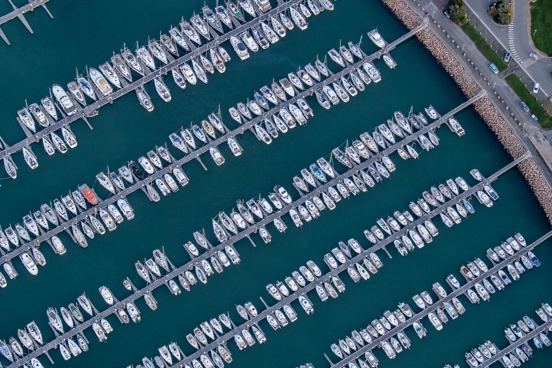 Alignement géométrique de bateaux de plaisance blancs amarrés aux pontons du port de Trébeurden vus du ciel.