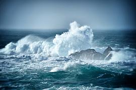 Écume blanche jaillissant contre des rochers sombres au milieu d’une mer agitée sous un ciel brumeux à Ouessant.