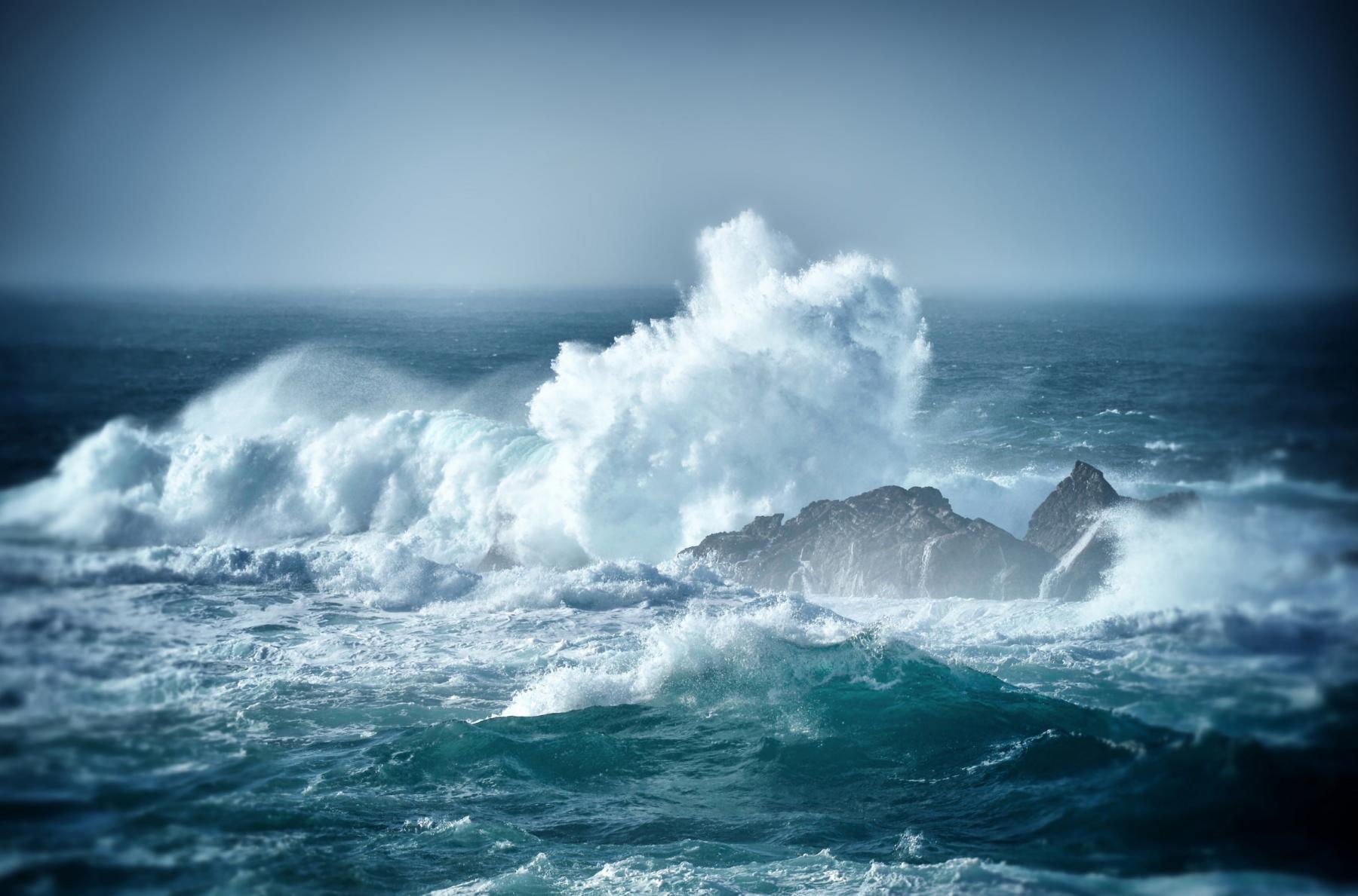 Écume blanche jaillissant contre des rochers sombres au milieu d’une mer agitée sous un ciel brumeux à Ouessant.
