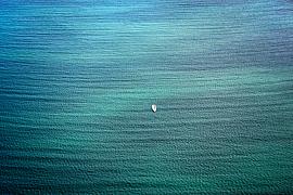 Vue de dessus d’un petit bateau blanc isolé sur une mer aux dégradés de bleu turquoise et de vert émeraude en Bretagne.