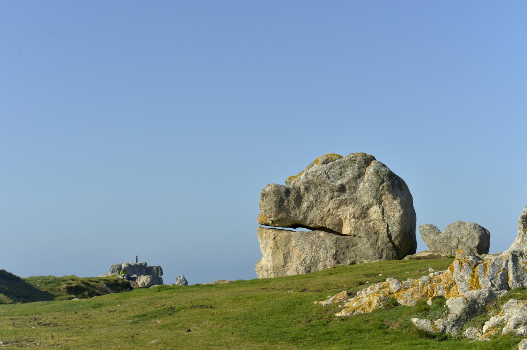 Gros rocher en forme de tête animale sur une lande d’herbe verte sous un ciel bleu à Ouessant en Bretagne.