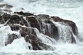 Écume blanche ruisselant en cascades sur des rochers sombres après le passage d’une vague puissante à Ouessant.