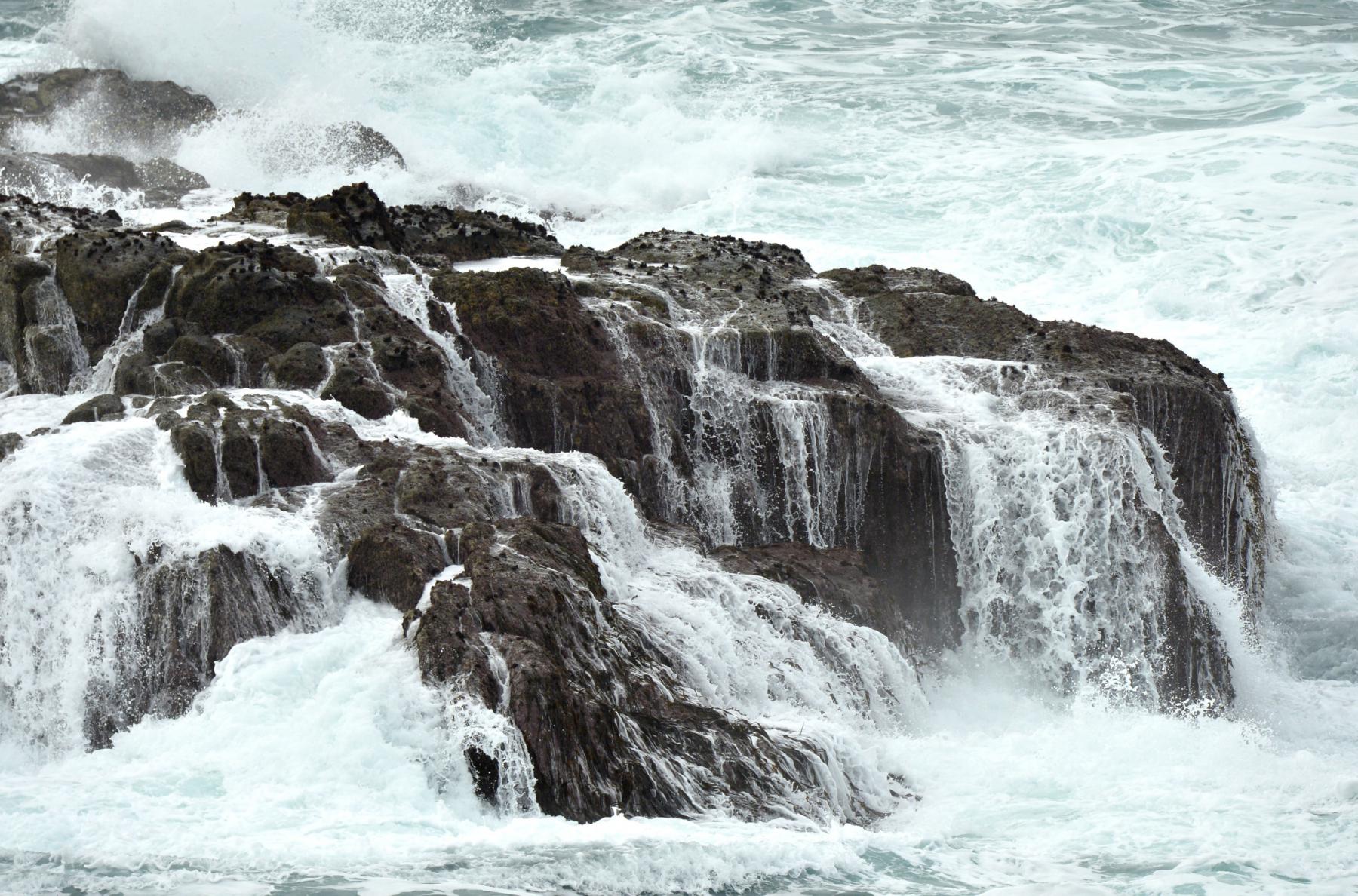 Écume blanche ruisselant en cascades sur des rochers sombres après le passage d’une vague puissante à Ouessant.
