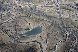 Vue aérienne de polders avec une mare de gabion entourée de chenaux d’eau et de traces dans la vase grise et beige.