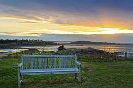 Banc en bois sur une pelouse verte face à la Manche, sous un ciel de coucher de soleil rayonnant à Saint-Briac.
