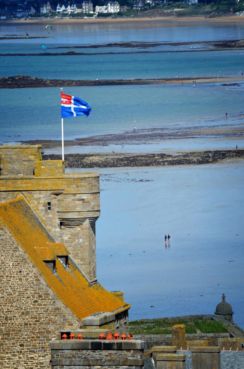 Drapeau de Saint-Malo sur les remparts historiques dominant la plage du Sillon et la mer à marée basse.
