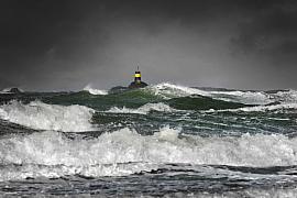 Grandes vagues d’écume blanche se brisant devant la balise Nerput jaune et noire sous un ciel glaz et sombre