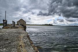Moulin à marée en pierre grise et digue sous un ciel orageux sur l’île d’Arz dans le Golfe du Morbihan.
