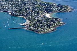 Vue aérienne de la pointe de Port Navalo montrant les maisons côtières, les jetées et les eaux bleues du Golfe du Morbihan.