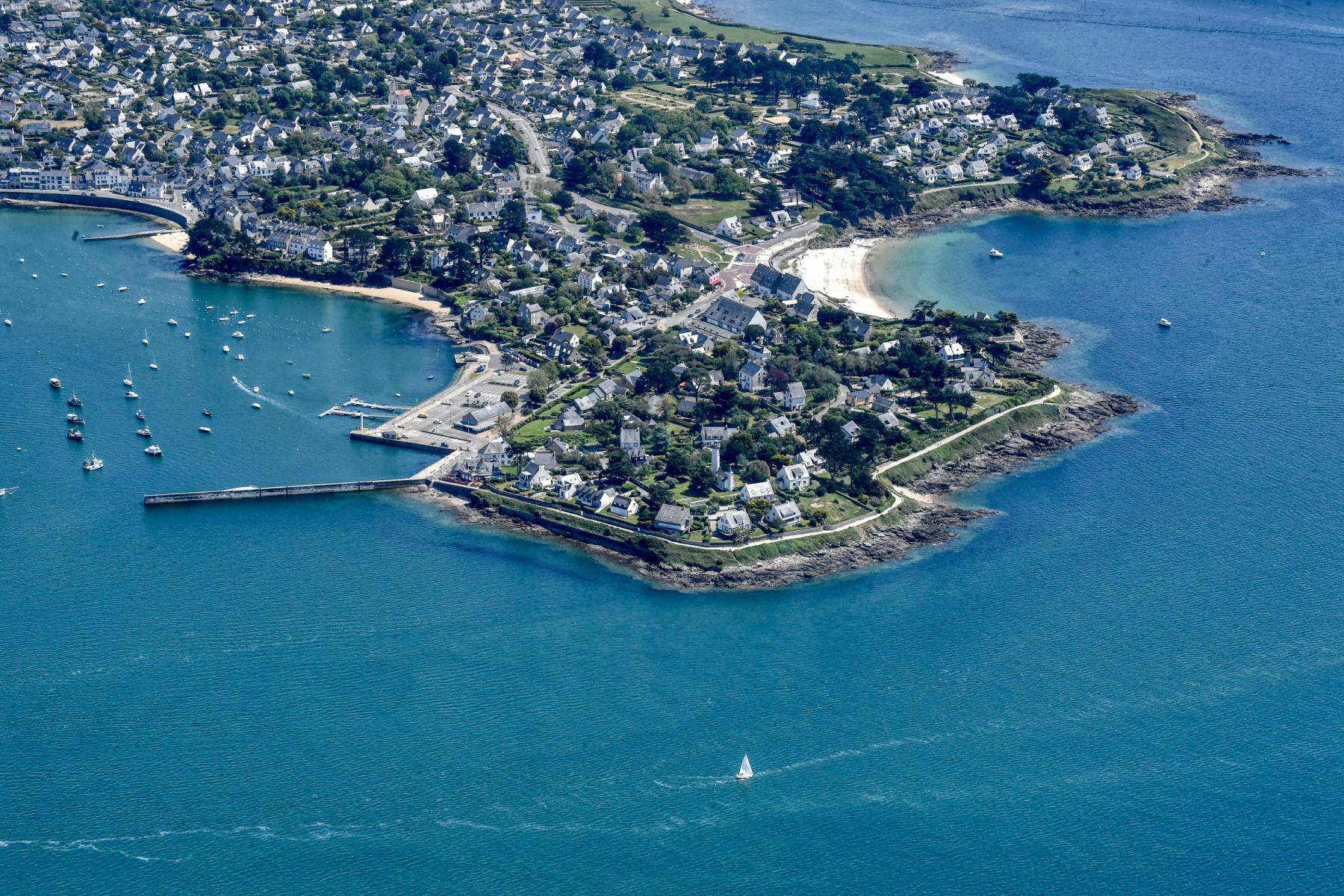 Vue aérienne de la pointe de Port Navalo montrant les maisons côtières, les jetées et les eaux bleues du Golfe du Morbihan.