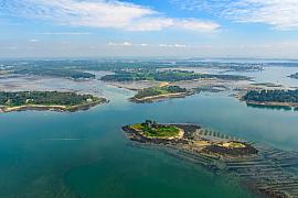 Vue aérienne sur les îles Ernic entourées d’eaux turquoise et de parcs à huîtres dans le Golfe du Morbihan sous un ciel azur.