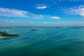 Eaux turquoise du Golfe du Morbihan entourant les îles d’Arz et de Lern sous un ciel bleu d’été parsemé de nuages.