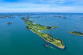 Vue aérienne panoramique de l’île aux Moines entourée des eaux bleues du Golfe du Morbihan sous un ciel clair ensoleillé.