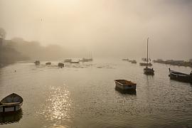 Plusieurs embarcations et voiliers isolés dans une brume épaisse et lumineuse sur les eaux calmes de Larmor Baden.