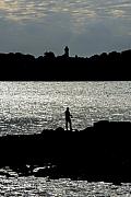 Silhouette de pêcheur sur les rochers devant la mer scintillante et le phare de Port-Navalo en arrière-plan.