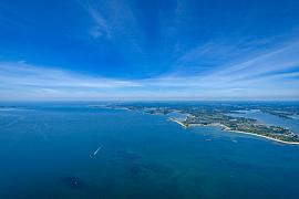 Vue d’avion du littoral breton avec mer turquoise, côtes découpées de Locmariaquer et sillage d’un bateau sous un ciel bleu azur.