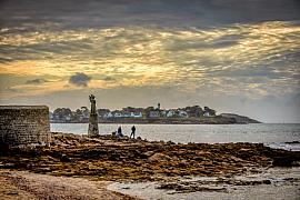 Statue de la Vierge sur un socle en pierre face à la mer à la pointe de Kerpenhir sous un ciel nuageux au crépuscule.