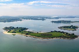 Île de Govihan verdoyante entourée d’eaux calmes bleutées avec parcs à huîtres visibles sous la surface à Sarzeau.