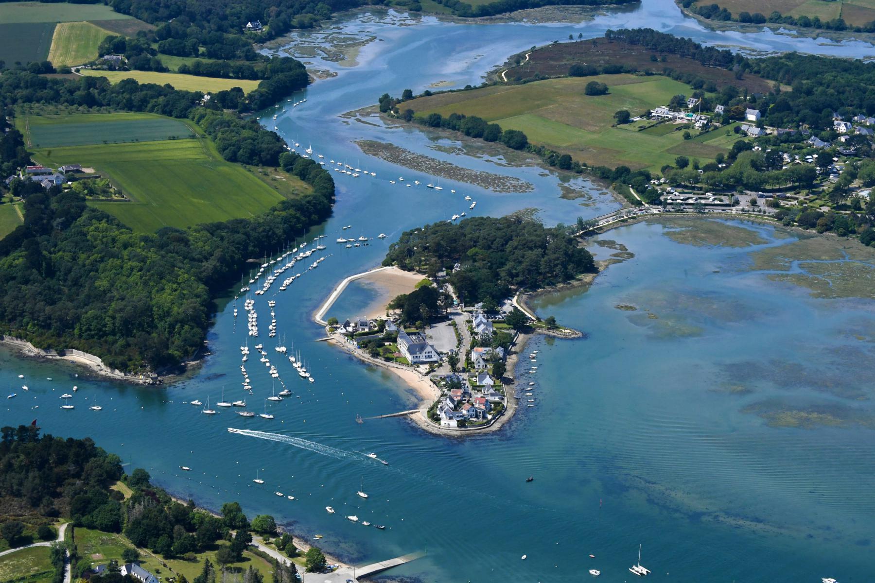 Vue de haut de la presqu’île de Conleau avec ses maisons blanches, entourée d’eaux bleues et de nombreux voiliers au mouillage.