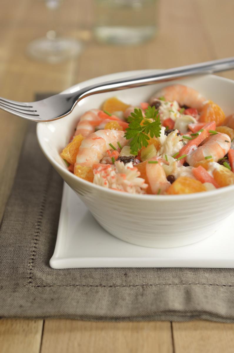 Salade de crevettes et agrumes dans un bol blanc strié avec fourchette en argent et herbes fraîches sur tissu gris.