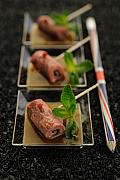 Trois verrines de carpaccio de bœuf roulé avec feuilles de menthe sur fond noir texturé, éclairage studio professionnel.