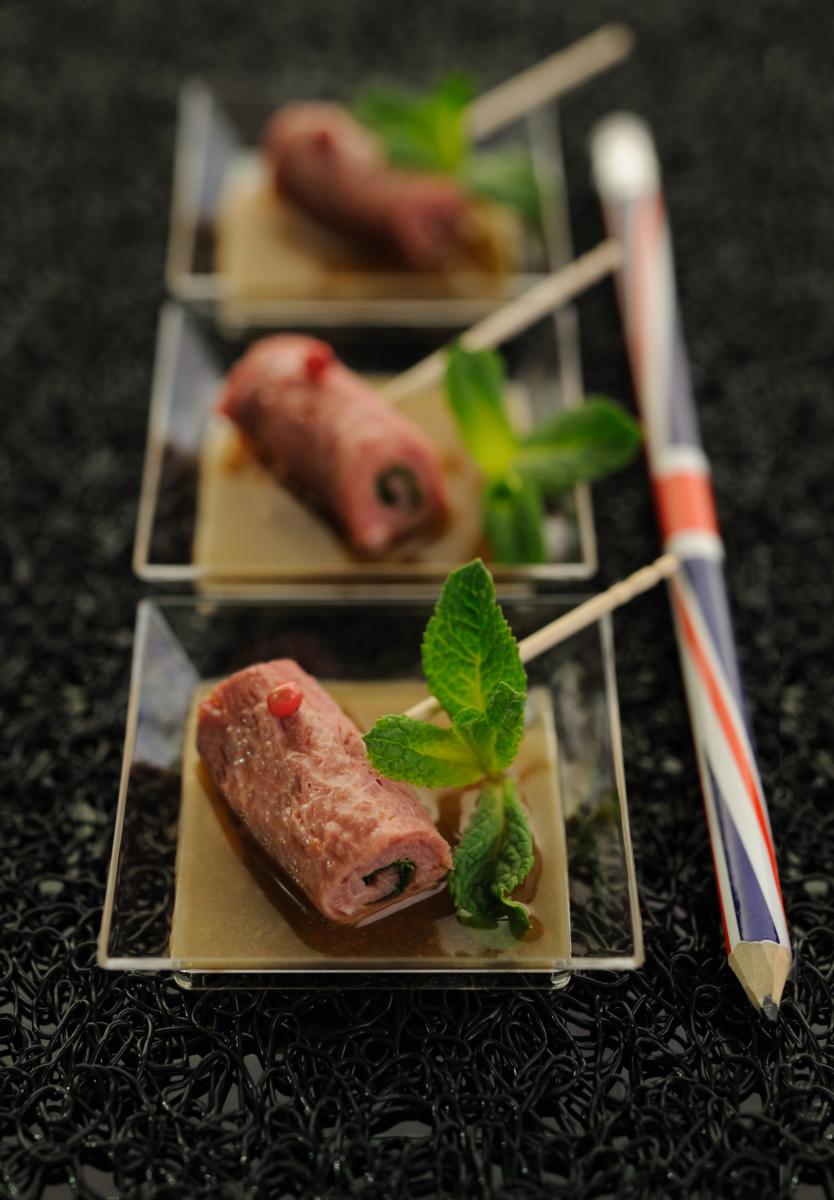 Trois verrines de carpaccio de bœuf roulé avec feuilles de menthe sur fond noir texturé, éclairage studio professionnel.
