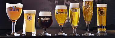 Sept verres de bières blondes, blanches et brunes avec mousse onctueuse, alignés sur une table sombre en studio.