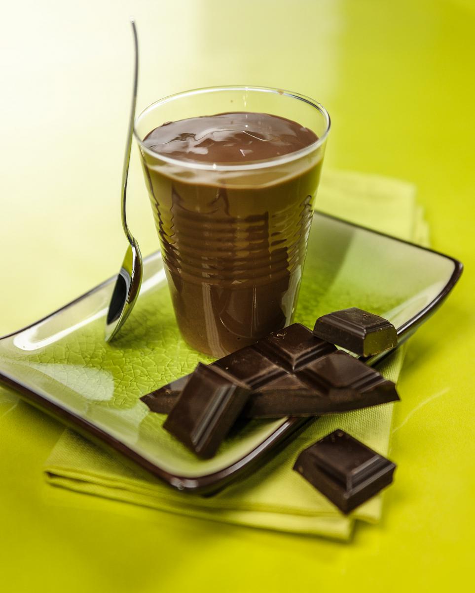 Crème dessert au chocolat onctueuse dans son verre, posée sur une assiette verte avec des carrés de chocolat noir 