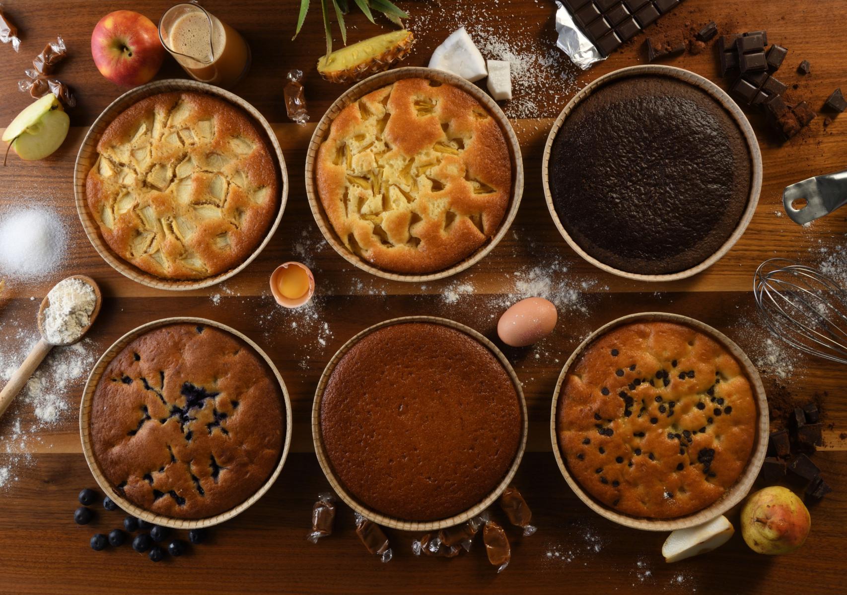 Vue de haut de six tartes sucrées sur bois avec farine œufs chocolat et fruits frais en décor culinaire.