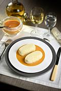 Quenelles sur sauce Nantua orange dans une assiette blanche, verres de vin blanc et saucière en arrière-plan lumineux.
