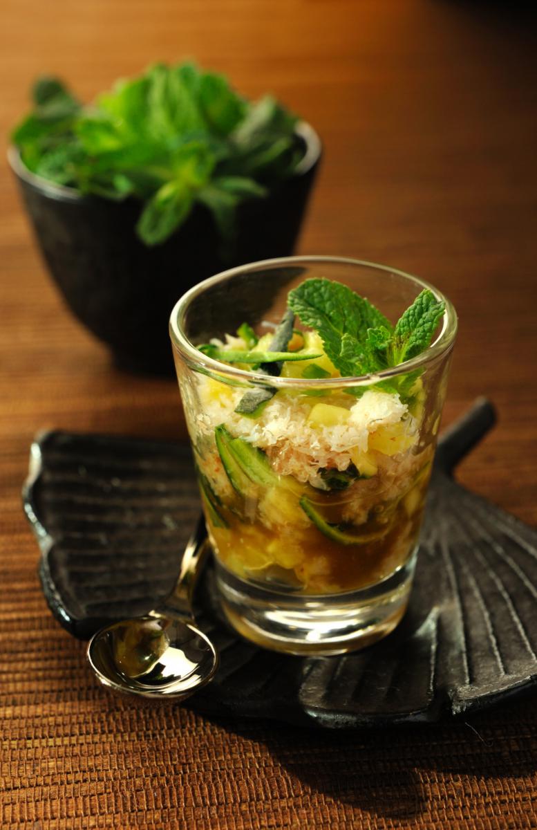Verrine transparente garnie de crabe et soja décorée de menthe fraîche sur un plat noir texturé sous une lumière chaude.