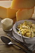 Assiette de pâtes aux artichauts et parmesan râpé sur une table en bois avec de larges blocs de fromage en arrière-plan.