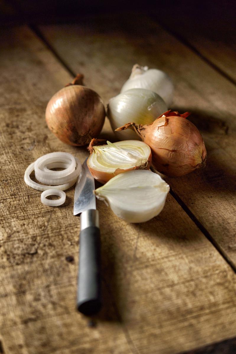 Oignons jentiers et émincés posés sur une planche en bois rustique avec un couteau d’office sous une lumière tamisée.
