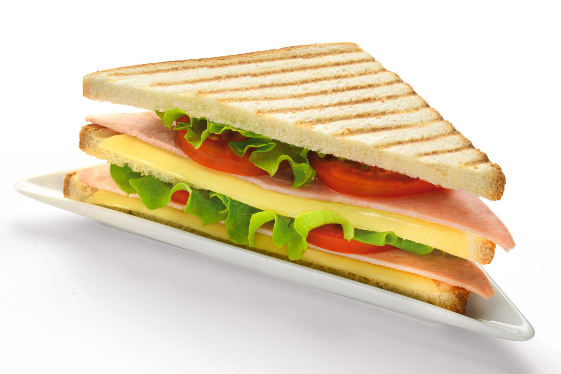 Sandwich triangle en pain de mie grillé garni de jambon fromage tomates et salade sur une assiette blanche épurée.