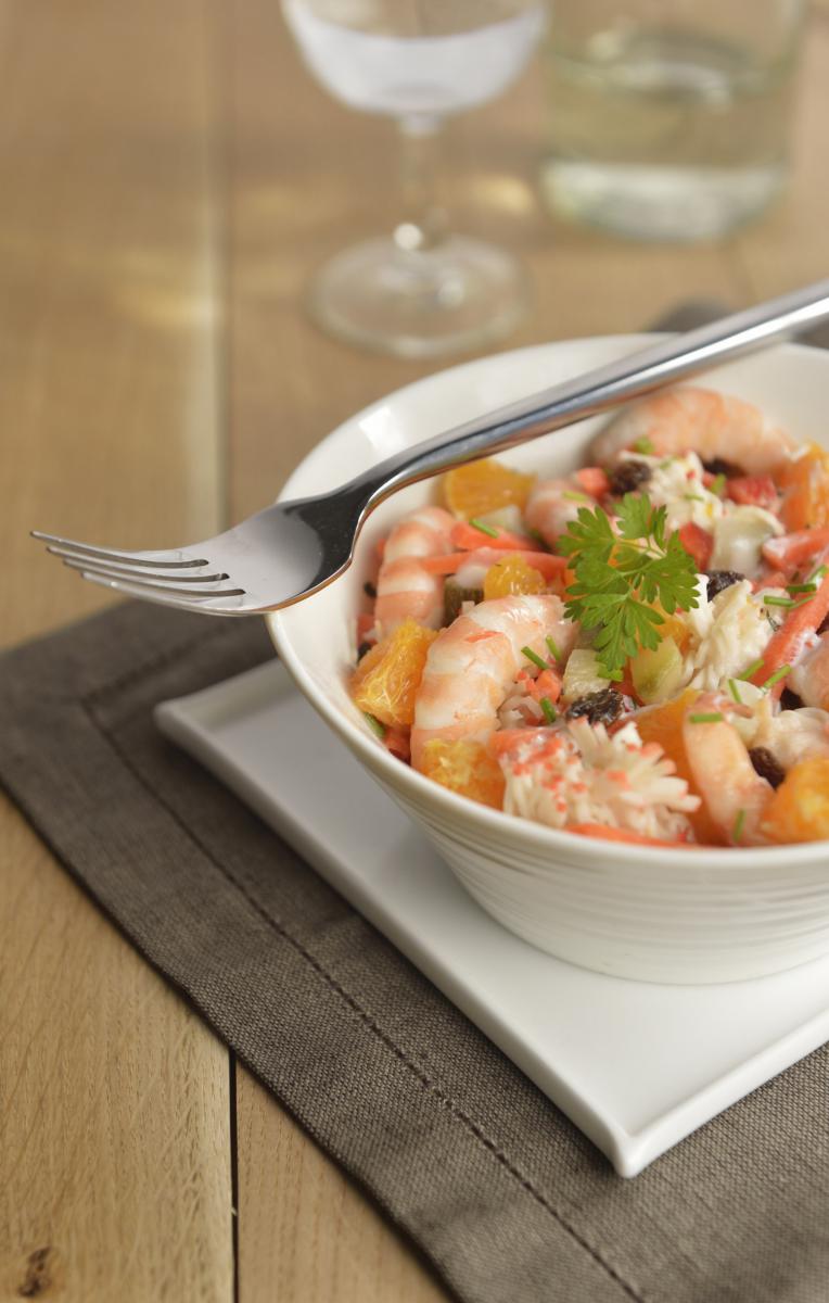 Bol de salade de gambas, surimi et quartiers d’oranges avec une fourchette posée sur le rebord, lumière naturelle.