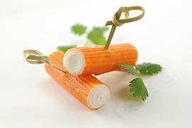 Deux bâtonnets de surimi orange et blanc avec piques en bambou et feuilles de coriandre fraîche sur fond blanc lumineux.