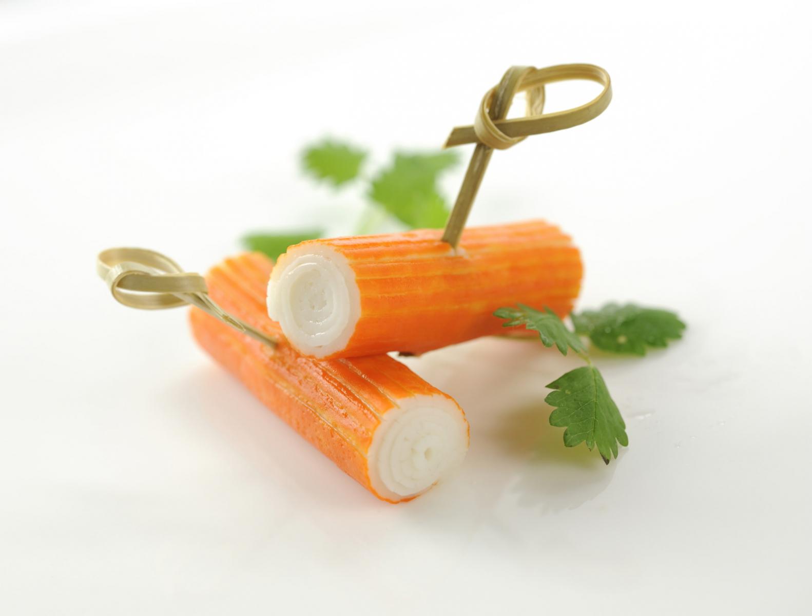 Deux bâtonnets de surimi orange et blanc avec piques en bambou et feuilles de coriandre fraîche sur fond blanc lumineux.