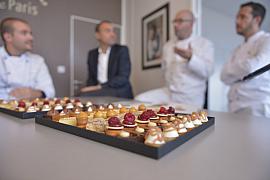 Plateaux de petits fours sucrés nets au premier plan devant des chefs en tenue de travail flous en arrière-plan.