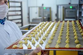Employé en tenue de protection portant un plateau de petits fours pochés dans un laboratoire industriel agroalimentaire.