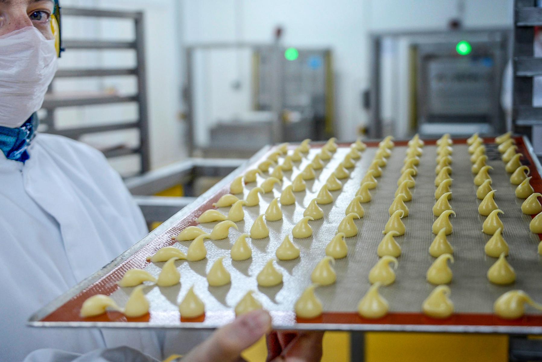 Employé en tenue de protection portant un plateau de petits fours pochés dans un laboratoire industriel agroalimentaire.