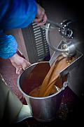 Coulée de chocolat liquide sortant d’une machine industrielle vers un seau en inox tenu par un opérateur en usine.