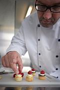 Chef pâtissier déposant une framboise sur une pièce cocktail sucrée lors d’une fabrication artisanale en Bretagne.